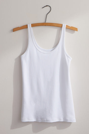 A plain white sleeveless tank top on a wooden hanger against a light-colored wall.