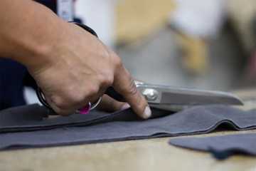 A person uses scissors to cut a piece of gray fabric on a table.