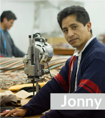 A man sits at a worktable beside a fabric-cutting machine, wearing a measuring tape around his neck. The name Jonny is displayed in large text in the foreground.