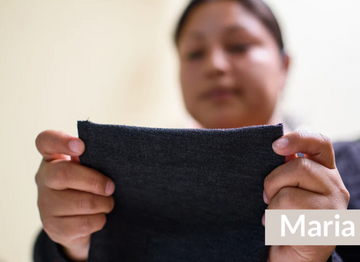 A person holds and examines a piece of dark fabric with both hands; the name Maria appears in the bottom right corner.