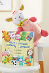 A plush pink and cream stuffed animal leans against a childrens book titled Meet the Joobles! ¬°Conoce a los Joobles! with colorful illustrated animal characters on the cover.