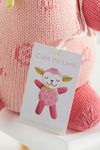 A close-up of a pink knitted stuffed animal with a tag that reads Cutie the Lamb and an illustrated lamb, branded with thejoobles.com.