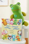 A green plush frog sits behind a childrens book titled Meet the Joobles! ¬°Conoce a los Joobles! by Monica Brown, featuring colorful illustrated animal characters on the cover.