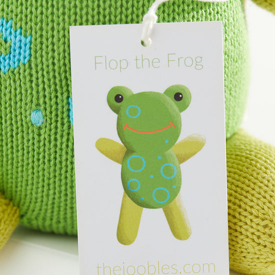 A tag reading Flop the Frog with an illustrated frog is attached to a green knitted toy. The website thejoobles.com is printed at the bottom of the tag.