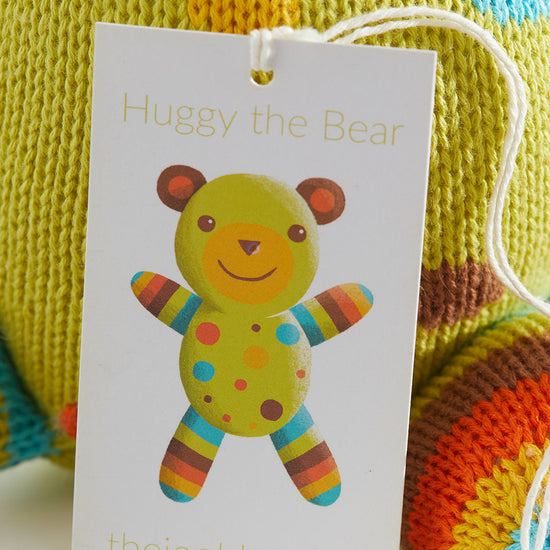 A product tag attached to a knitted toy reads Huggy the Bear with a picture of a colorful bear and the website thejoobles.com below.
