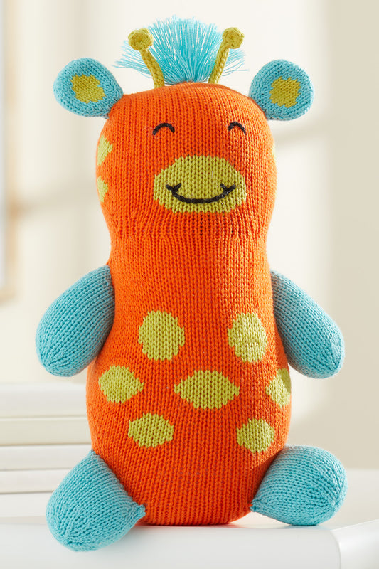 A knitted stuffed toy giraffe with an orange body, blue limbs and ears, yellow spots, a smiling face, and blue yarn hair on top.