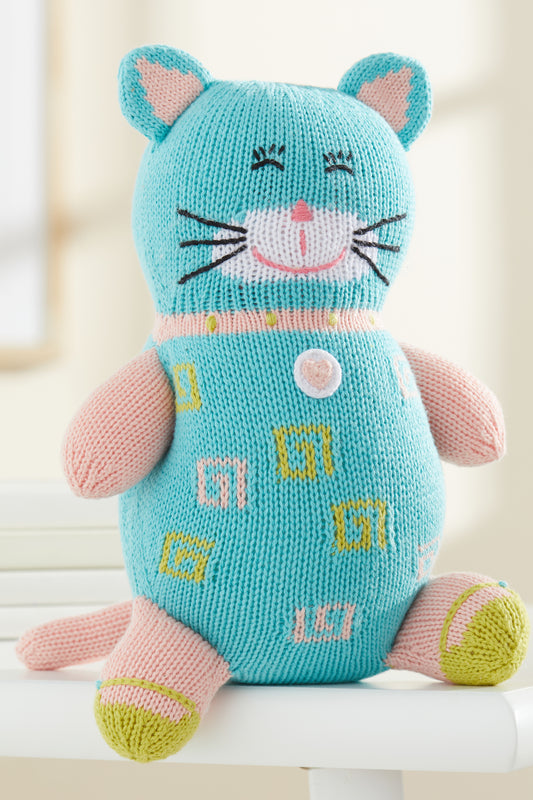 A knitted stuffed cat toy with blue and pink yarn, embroidered facial features, and patterned designs on its body, sitting upright on a white surface.