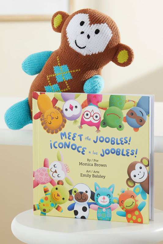 A knitted toy monkey leans against a colorful childrens book titled Meet the Joobles! featuring illustrated animal characters on the cover.