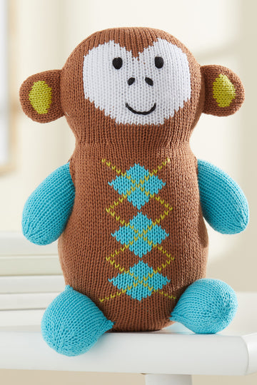 A knitted stuffed monkey with a brown body, blue arms and legs, yellow and green diamond pattern on its chest, and a white face with a smiling expression.
