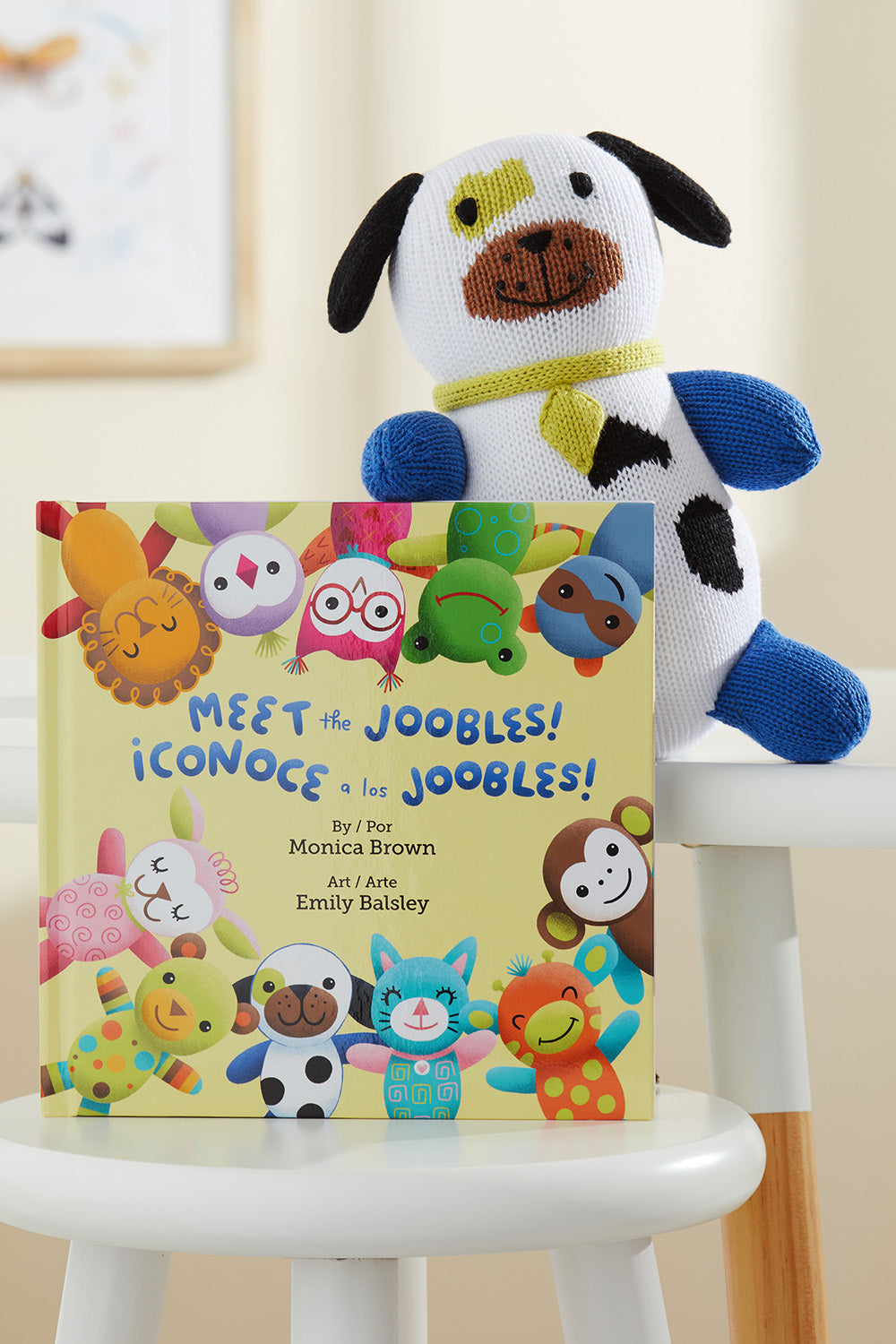 A bilingual childrens book titled Meet the Joobles! ¬°Conoce a los Joobles! is propped on a white chair next to a knit plush dog.