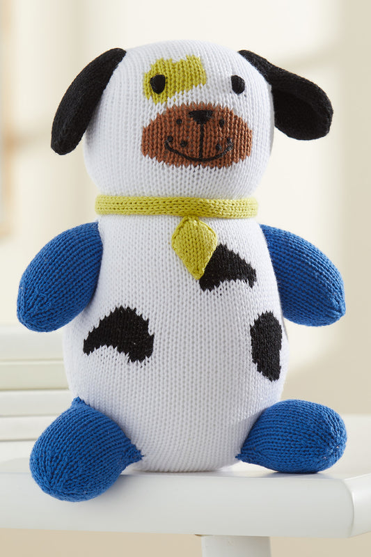 A knitted plush dog toy with blue limbs, black spots, a yellow collar, and a brown snout, sitting on a white surface.