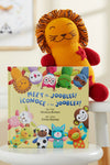A knit lion plush toy sits behind a childrens book titled Meet the Joobles! ¬°Conoce a los Joobles! featuring colorful illustrated animal characters on the cover.