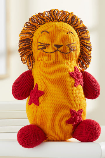 A knitted stuffed lion toy with a yellow body, red arms and legs, red star patterns, and a mane made of orange and brown yarn.