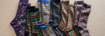 A row of colorful patterned socks with various stripes and geometric designs, laid out flat on a neutral surface.