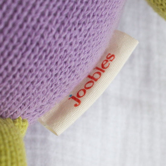 Close-up of a fabric tag labeled joobles attached to a knitted item in purple and green colors.