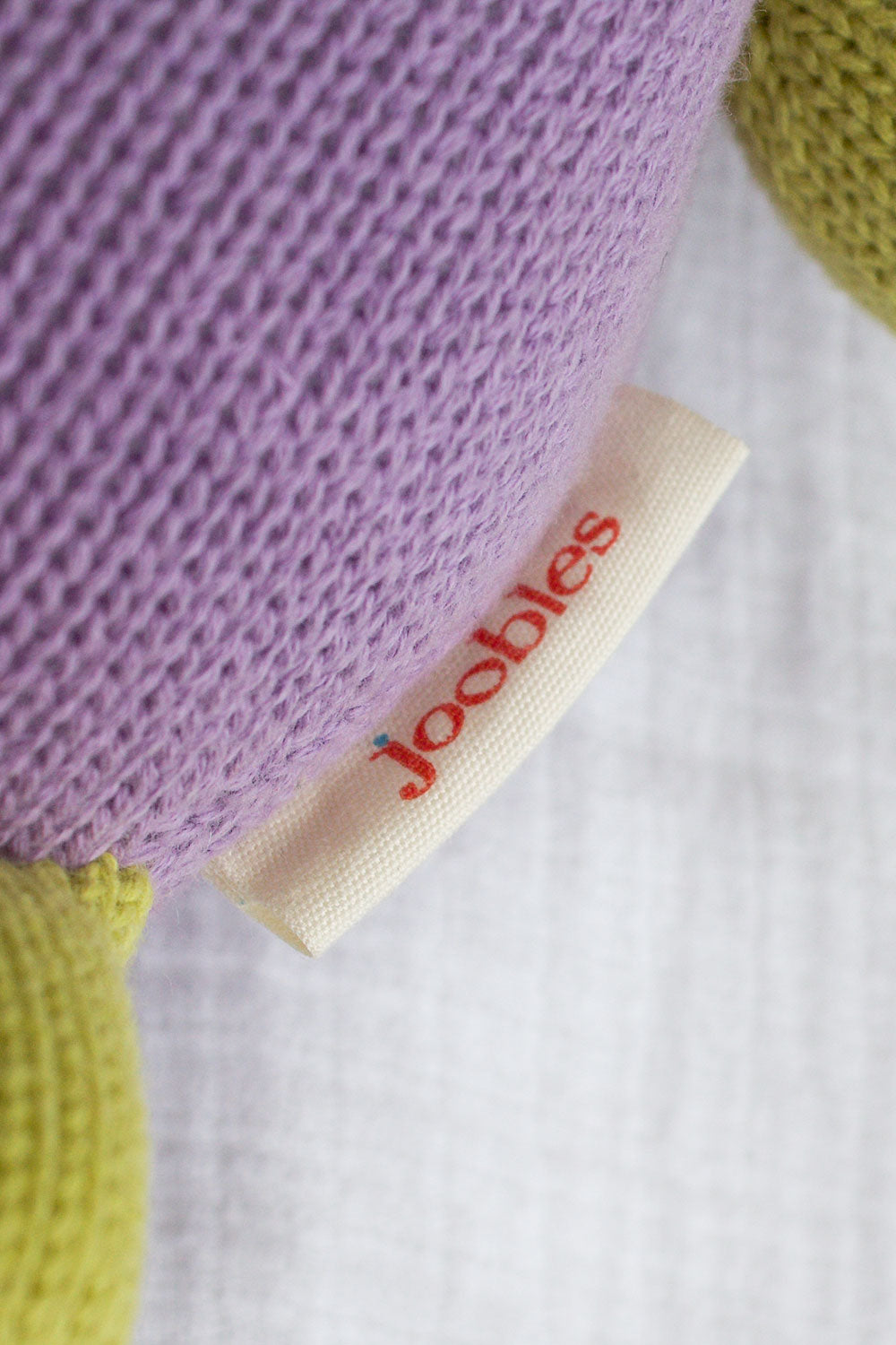 Close-up of a fabric tag labeled joobles attached to a knitted item in purple and green colors.