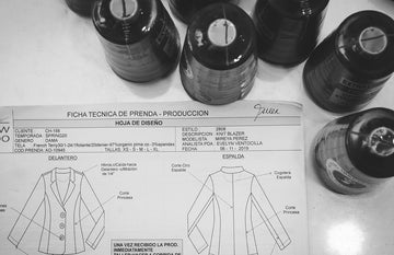 Black and white photo of a garment technical sheet for a blazer, with sewing thread spools arranged above the document.