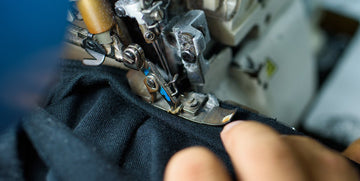 Close-up of a sewing machine stitching black fabric with a persons hand guiding the material.