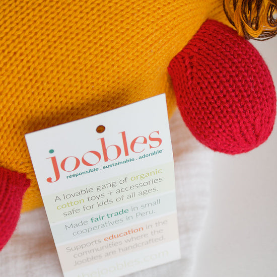 A product tag attached to a knitted toy reads: joobles: responsible, sustainable, adorable and describes the toy as organic, fair trade, and supports education.