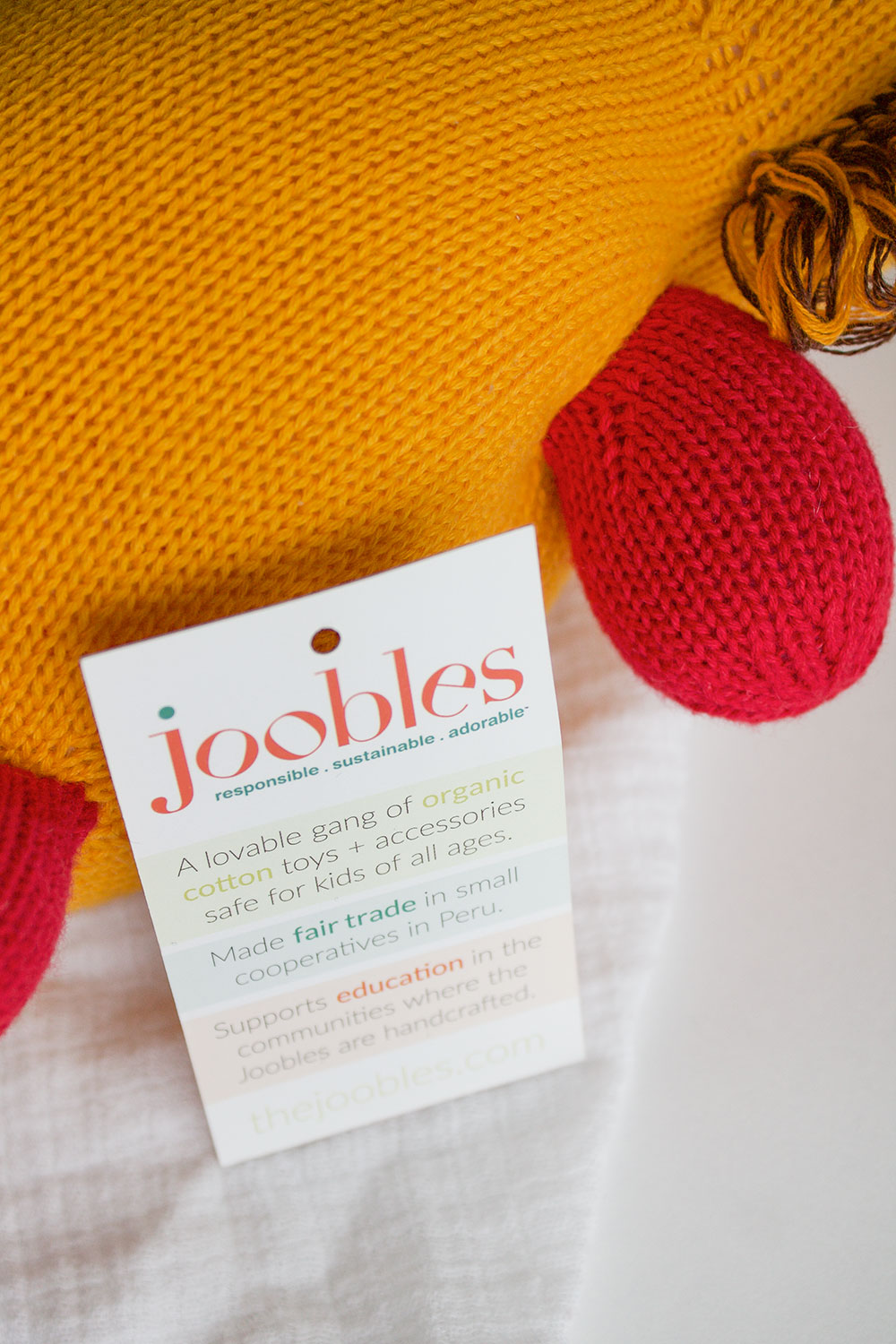 A product tag attached to a knitted toy reads: joobles: responsible, sustainable, adorable and describes the toy as organic, fair trade, and supports education.